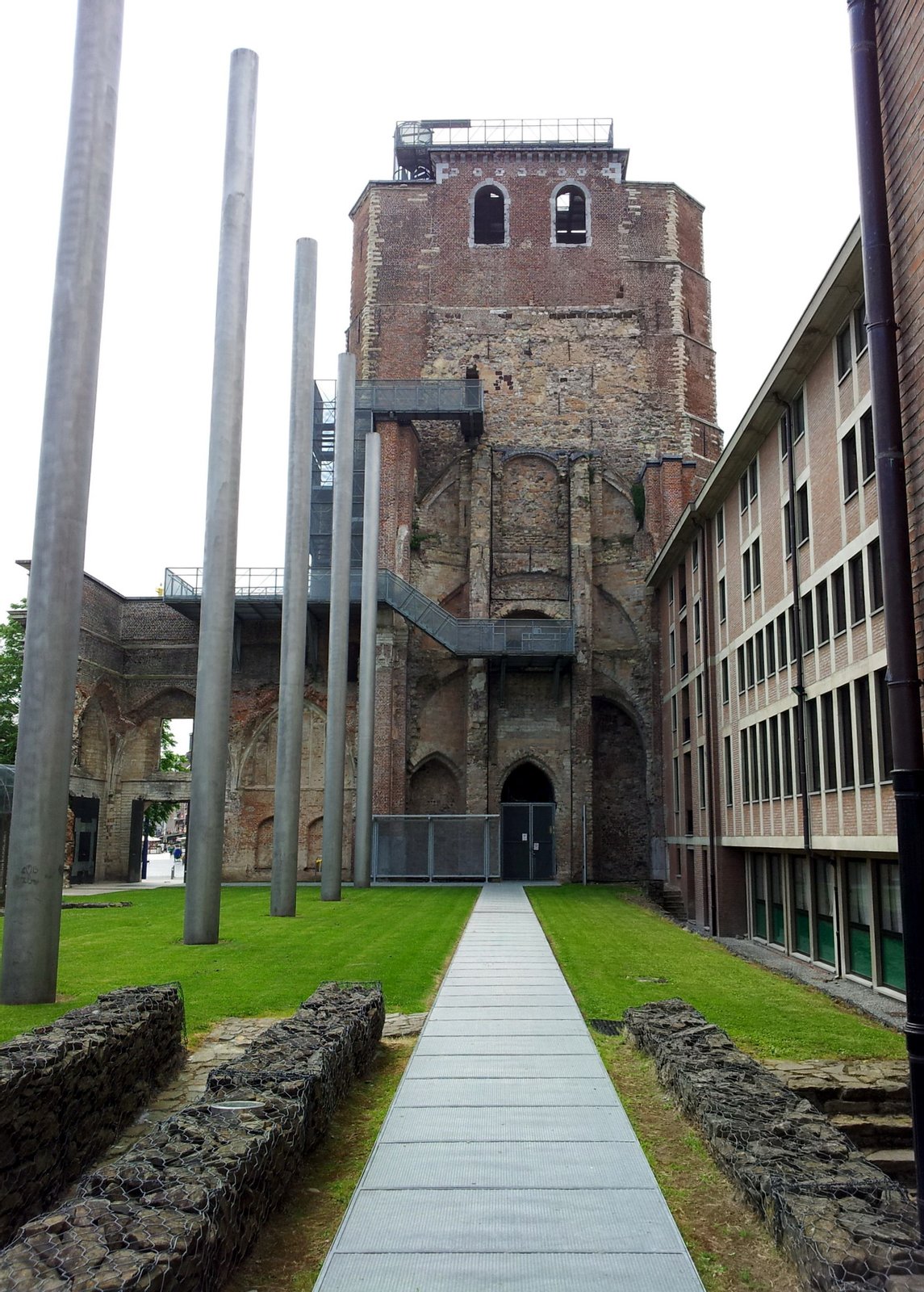 View from the North of the tower of the demolished abbey church of the former Benedictine abbey in Sint-Truiden, Belgium. The poles on the left indicate the approximate height of the church. The slope on the left is the present entrance to the crypt. | Sint-Truiden in Belgium