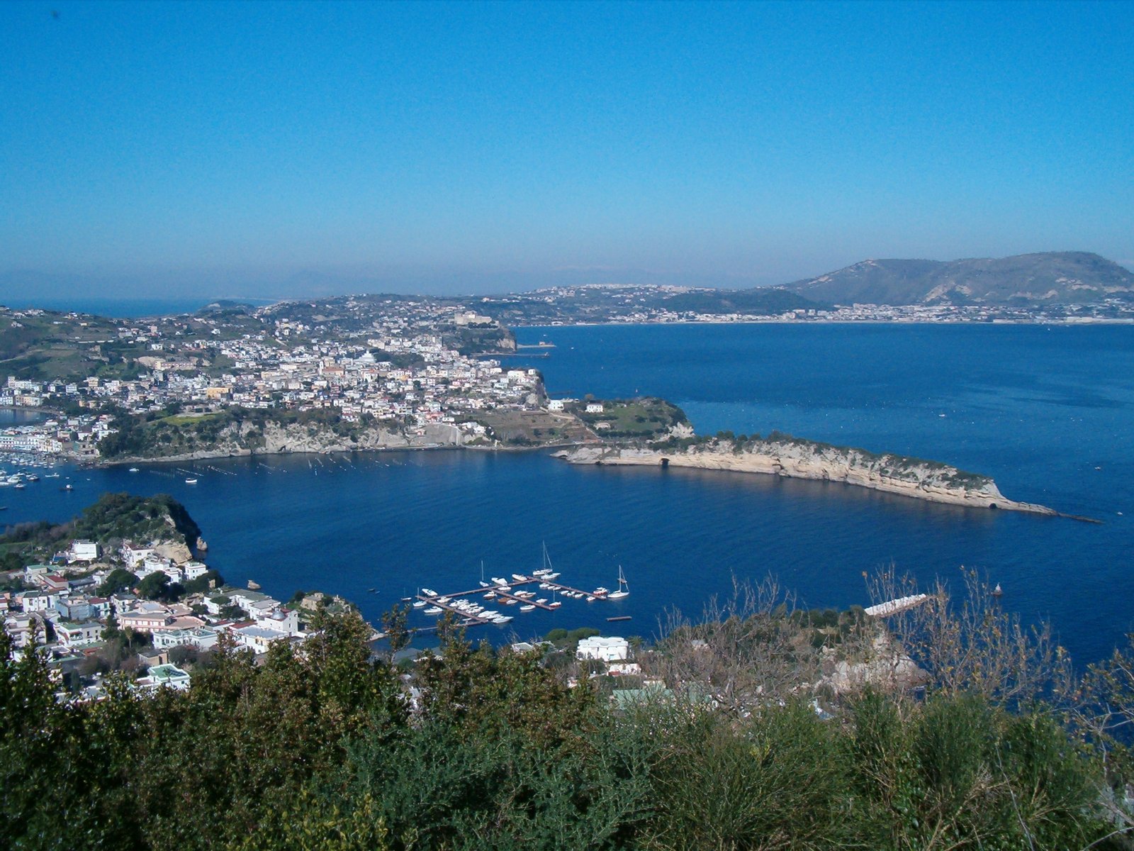 Comune di Bacoli - Veduta da Capo Miseno sul Porto di Miseno che è l'antico vulcano del cui cratere si conserva il bordo nella lunga isola chiamata Punta Pennata. In basso a sinistra, si vede il villaggio di Miseno, frazione del comune di Bacoli il quale si trova di fronte sulla terraferma. | Bacoli in Italy